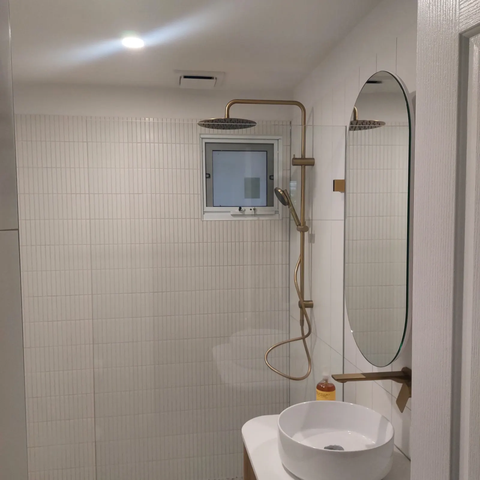 Powder room with brass shower and oval mirror