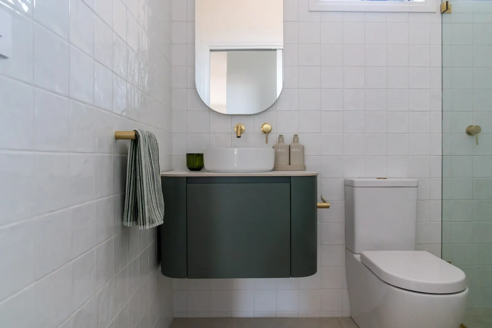 Editorial bathroom with curved green vanity and brass tapware